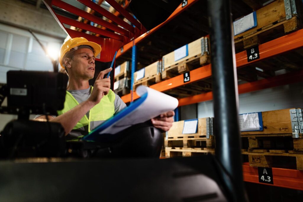 pensive-forklift-operator-examining-stock-packages-shelves-warehouse